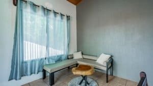 Bright living room with large window, blue curtains, and simple furniture.