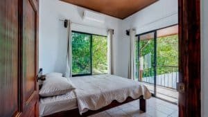 Bright bedroom with large windows and balcony overlooking lush greenery in Dominical.