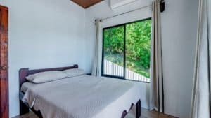 Bedroom with large window overlooking lush green trees in Dominical.