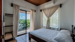 Bright bedroom with large windows and balcony overlooking greenery.