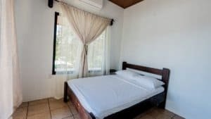 Simple bedroom with a bed, window, and curtains in Dominical, Costa Rica.