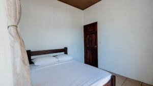 Simple bedroom with white walls, wooden door, and bed with white linens.