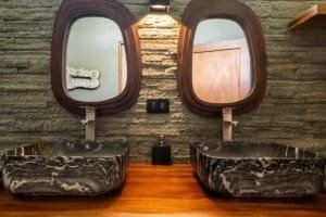 Modern bathroom with two marble sinks, wooden mirrors, and stone wall in Uvita.