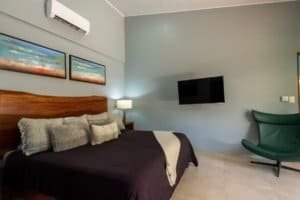 Modern bedroom in Uvita with bed, wall art, TV, and green chair.
