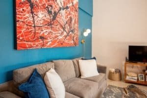 Modern living room with beige sofa, colorful artwork, and blue accent wall.
