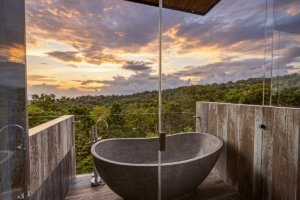 Modern outdoor bathtub overlooking lush Costa Rican forest at sunset.