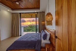 Bedroom with ocean view, wooden accents, and sunset scenery.