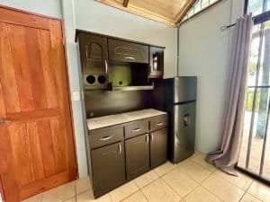 Interior of a small Costa Rican cabin kitchen with black cabinets and fridge.