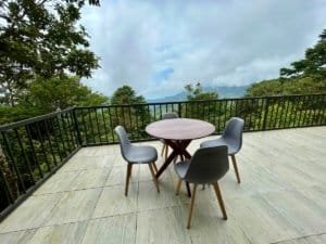 Outdoor balcony with table and chairs overlooking lush forest and ocean in Dominical.