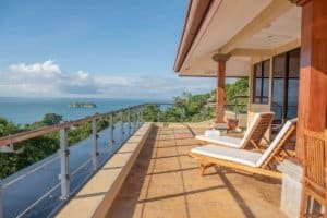 Balinese-inspired home balcony with ocean view and lounge chairs.