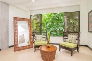 Indoor seating area with two chairs and a mirror overlooking tropical greenery.