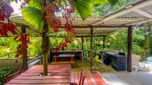 Outdoor covered patio with kitchen, dining, and lush tropical garden.