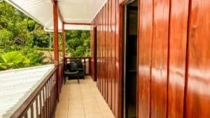 Balcony of a Costa Rican style home with wooden walls and lush greenery view.