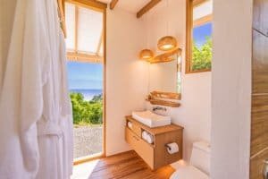 Bright bathroom with ocean view, wooden accents, and rainforest scenery.