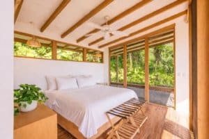 Bright bedroom with large windows overlooking lush rainforest in Costa Rica.