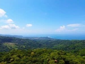Scenic ocean view from Dominical with lush green forest and blue sky.