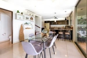 Bright dining area with glass table, modern decor, and open kitchen view.