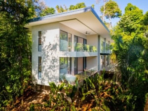 Contemporary tropical house with large windows and balcony in lush greenery.
