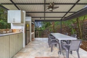 Covered outdoor dining space with table, chairs, and lush forest view.