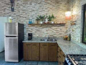 Costa Rican kitchen with wooden cabinets, granite countertop, and stainless steel refrigerator.