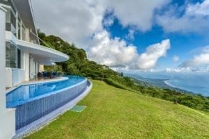 Modern house with infinity pool overlooking lush green hills and ocean.