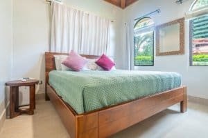Cozy bedroom with wooden bed, pink pillows, and tropical views in Dominical.