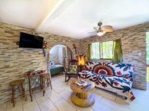 Living room in Dominical condo with colorful sofa, stone wall, and TV.