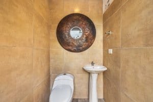 Contemporary bathroom with beige tiles, round mirror, toilet, and sink.