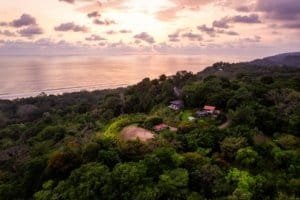 Lush green hillside with houses overlooking the ocean at sunset in Dominical.