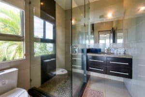 Contemporary bathroom with glass shower, modern vanity, and tropical view.