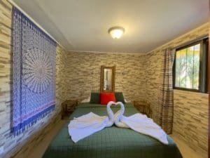 Bedroom with swan towel art, stone wall, and window view in Dominical.