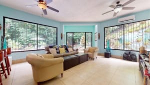 Spacious living room with large windows, comfortable seating, and tropical decor.