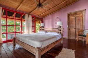 Bedroom with wooden furniture, pink walls, and ocean view in Dominical.