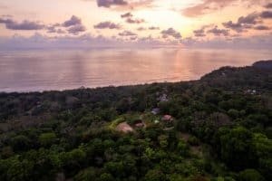Aerial view of lush green coastal estate with sunset over the ocean in Dominical.
