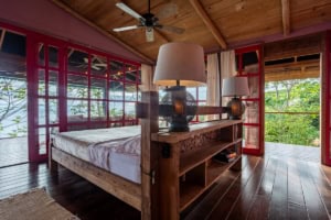 Bedroom with wooden furniture and large windows overlooking lush greenery.