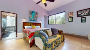 Bright bedroom with large window, colorful bedding, and cozy seating area.
