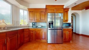Modern kitchen with wooden cabinets, stainless steel fridge, and large window.