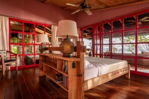 Bedroom with large windows overlooking lush greenery and ocean in Dominical.