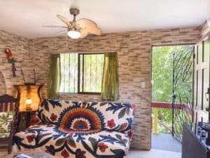 Living room with stone wall, green curtains, and balcony view in Dominical.