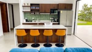 Contemporary kitchen with green tile backsplash, island, and four orange bar stools.