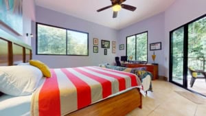 Bright bedroom with large windows, balcony, and colorful decor.