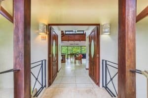 Interior view of a tropical villa entrance with wooden doors and lush greenery visible inside.