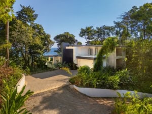 Modern tropical home with ocean view, lush greenery, and driveway in Dominical.