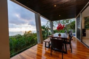 Balcony of a modern jungle home with ocean view and lush greenery.