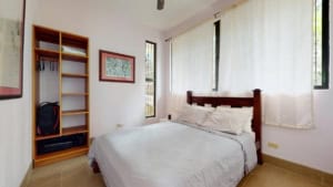 Bright bedroom with large windows, white curtains, and wooden furniture in Dominical.