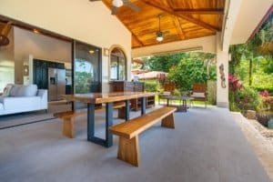 Covered outdoor patio with wooden ceiling, dining table, and lush garden view.