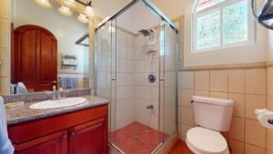 Bathroom of a Spanish Colonial-style home with shower, toilet, and wooden vanity.