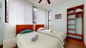 Bright bedroom with two beds, wooden furniture, and large windows in Dominical.