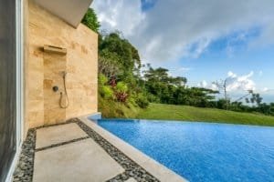 Modern outdoor shower with ocean view and lush jungle backdrop.
