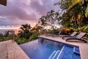Luxury jungle home with pool, lounge chairs, and panoramic ocean view.